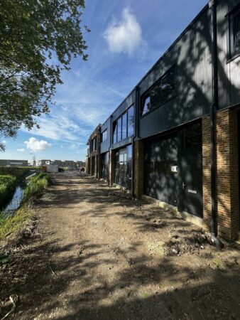 Nieuwbouwpand aan Broekdijk West met industriële gevel en onverharde oprit langs een sloot.